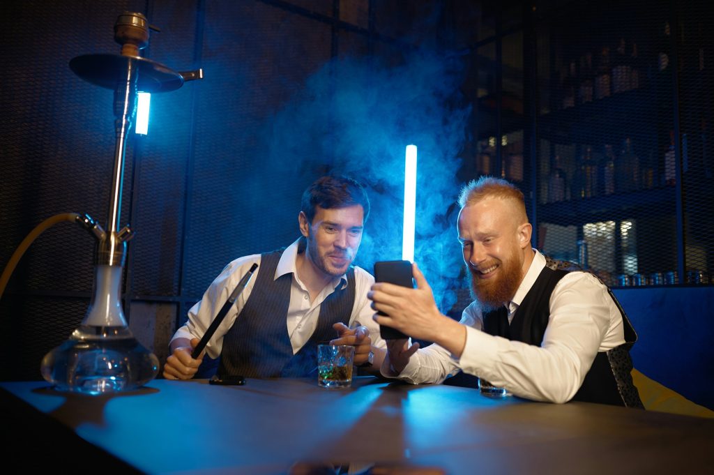Friends smoking hookah, drinking whisky and watching video on phone
